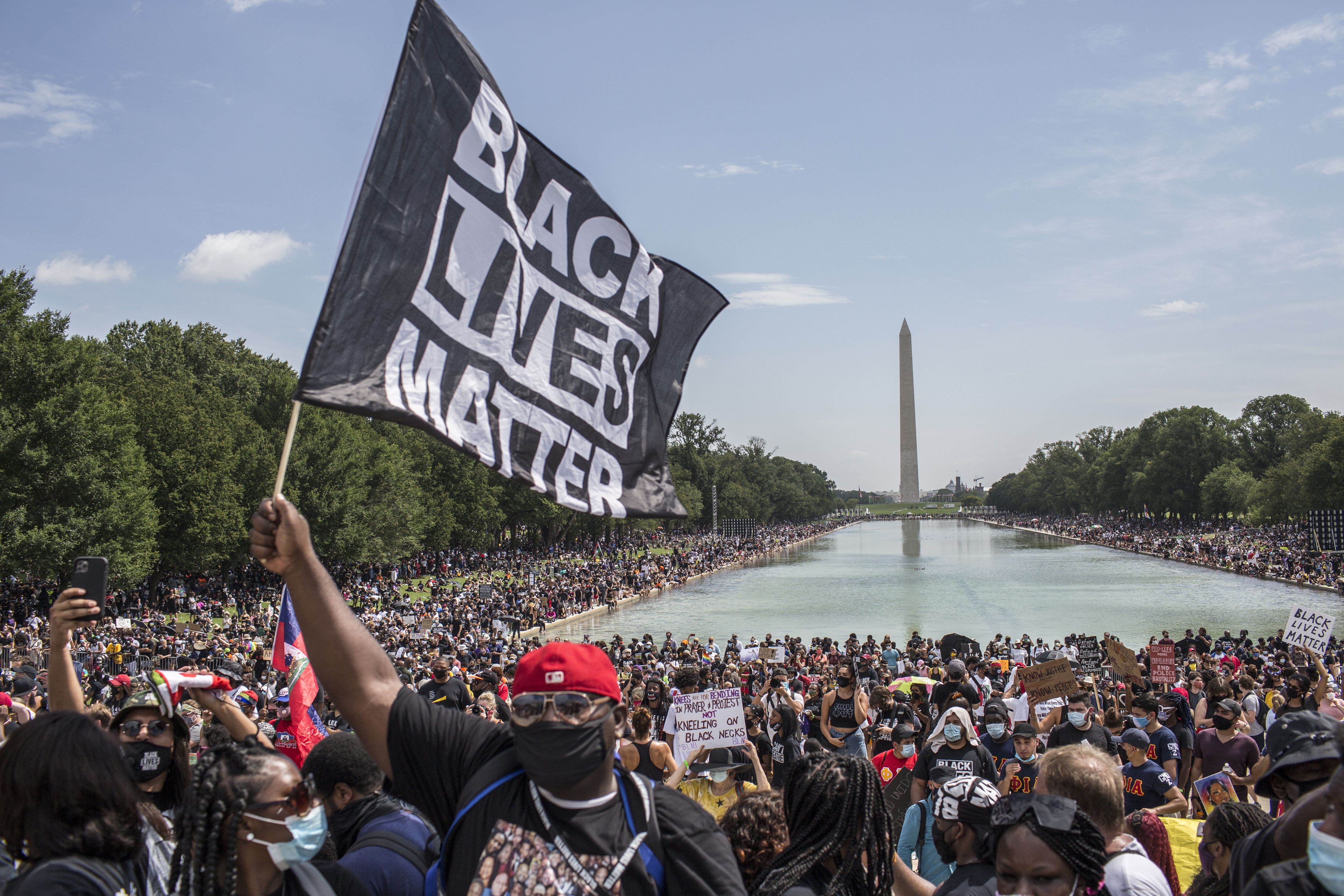 WASHINGTON, DISTRICT OF COLUMBIA, UNITED STATES - 2020/08/28: A demonstrator holding a flag with Black Lives Matter written on it while attending  the "Commitment March: Get Your Knee Off Our Necks" protest against racism and police brutality at the Lincoln Memorial in Washington, DC. The march coincides with the 57th anniversary of Martin Luther King, Jr.’s March on Washington, where he delivered his “I Have A Dream” speech in 1963. (Photo by Probal Rashid/LightRocket via Getty Images)