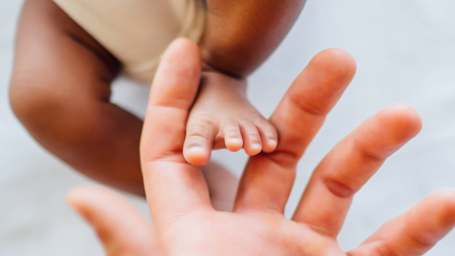 Close-up of parent hand touching newborn daughter's foot on bed