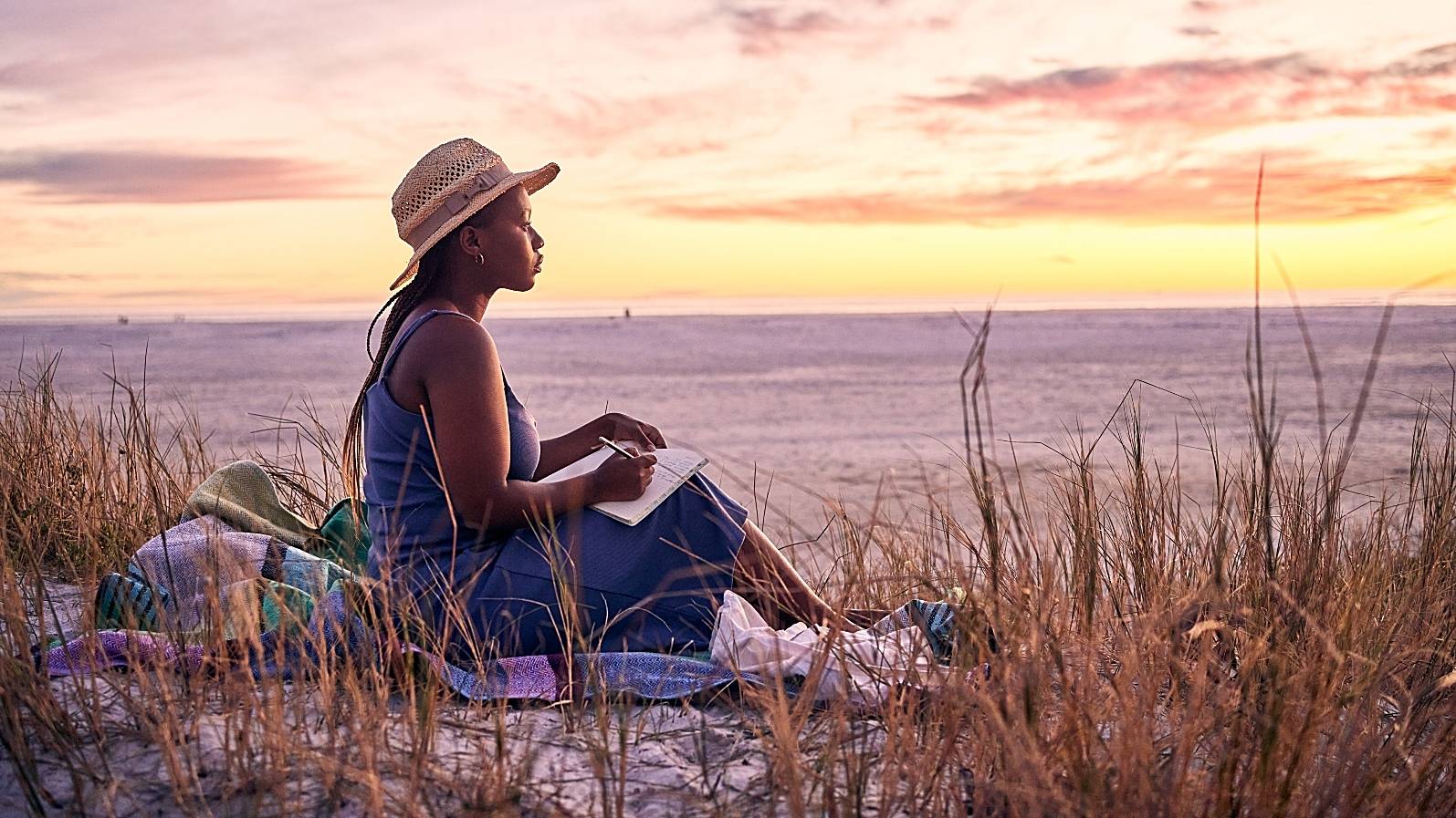 Shot of a young woman writing in her journal at the beach  