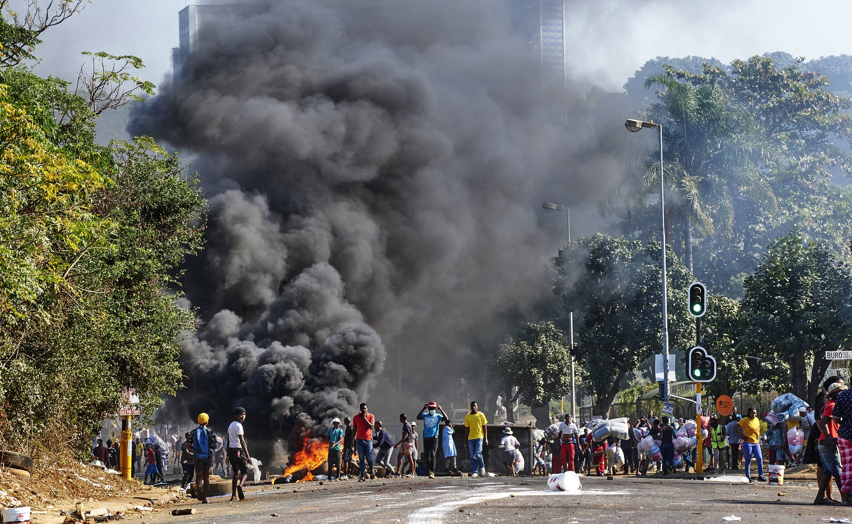 Looters outside a shopping centre alongside a burning barricade in Durban, South Africa, Monday July 12, 2021. Police say six people are dead and more than 200 have been arrested amid escalating violence during rioting that broke out following the imprisonment of South Africa's former President Jacob Zuma. (AP Photo/Andre Swart)