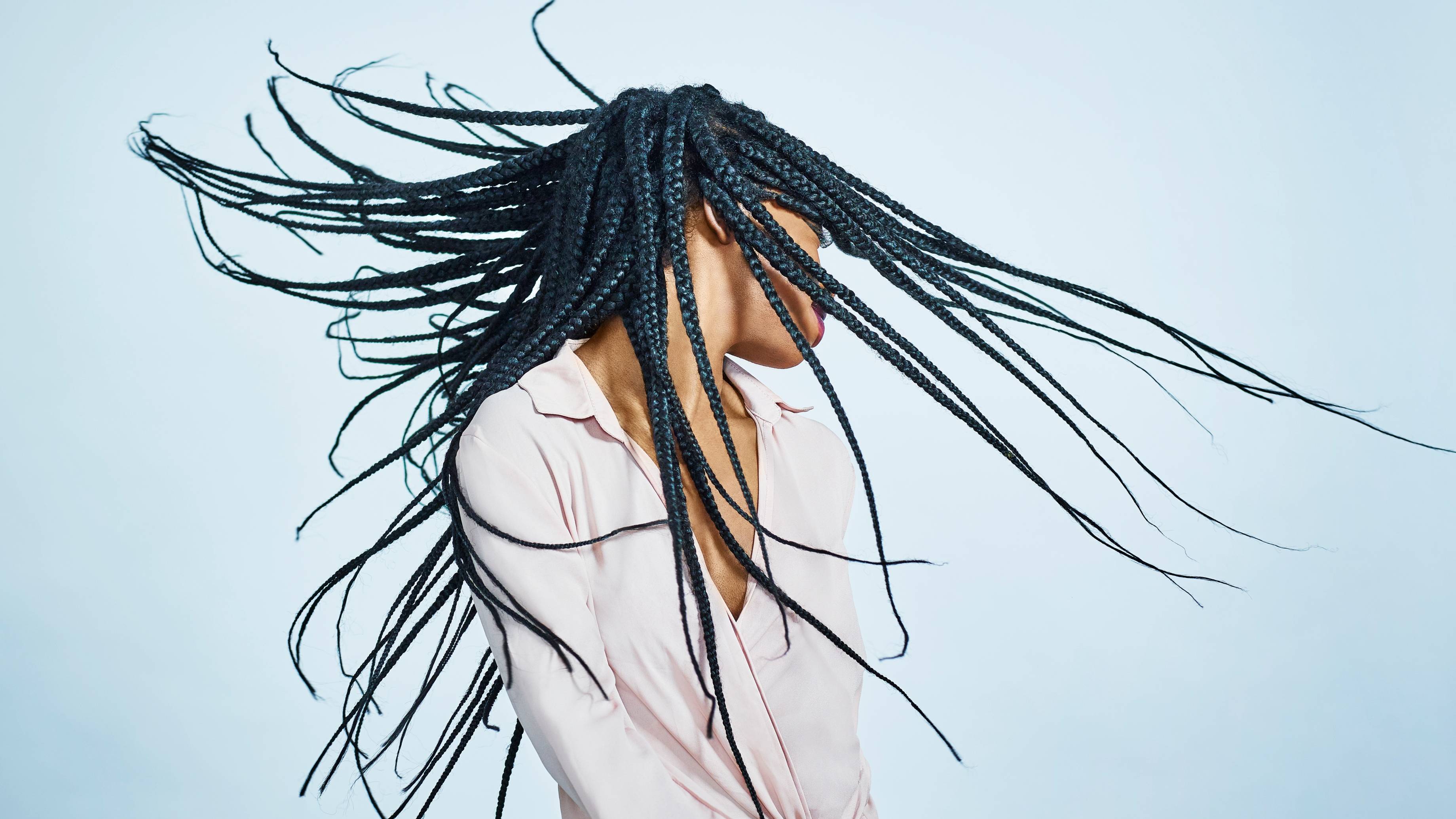 Portrait of young black female wearing pale pink blouse, flicking her braided hair.