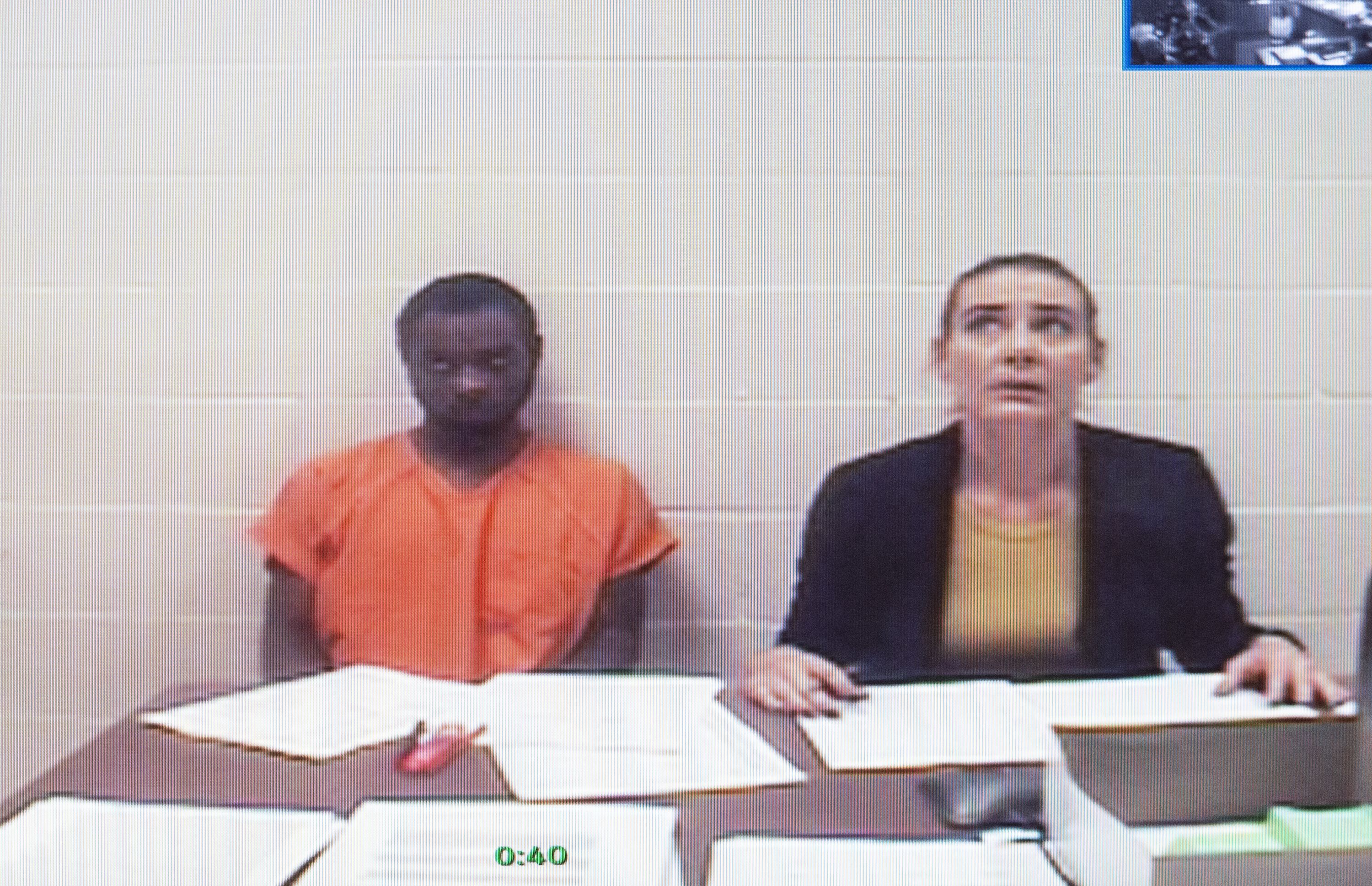 Tevin Biles-Thomas, left, shown on a video monitor, listens to his arraignment with public defender Alonda Bush from the Cuyahoga County jail as the hearing is held in Common Pleas Court in Cleveland, Friday, Sept. 13, 2019. Biles-Thomas is accused of killing three people at a New Year's Eve party in 2018 and is the older brother of U.S. Olympic gymnast Simone Biles. (AP Photo/Phil Long)