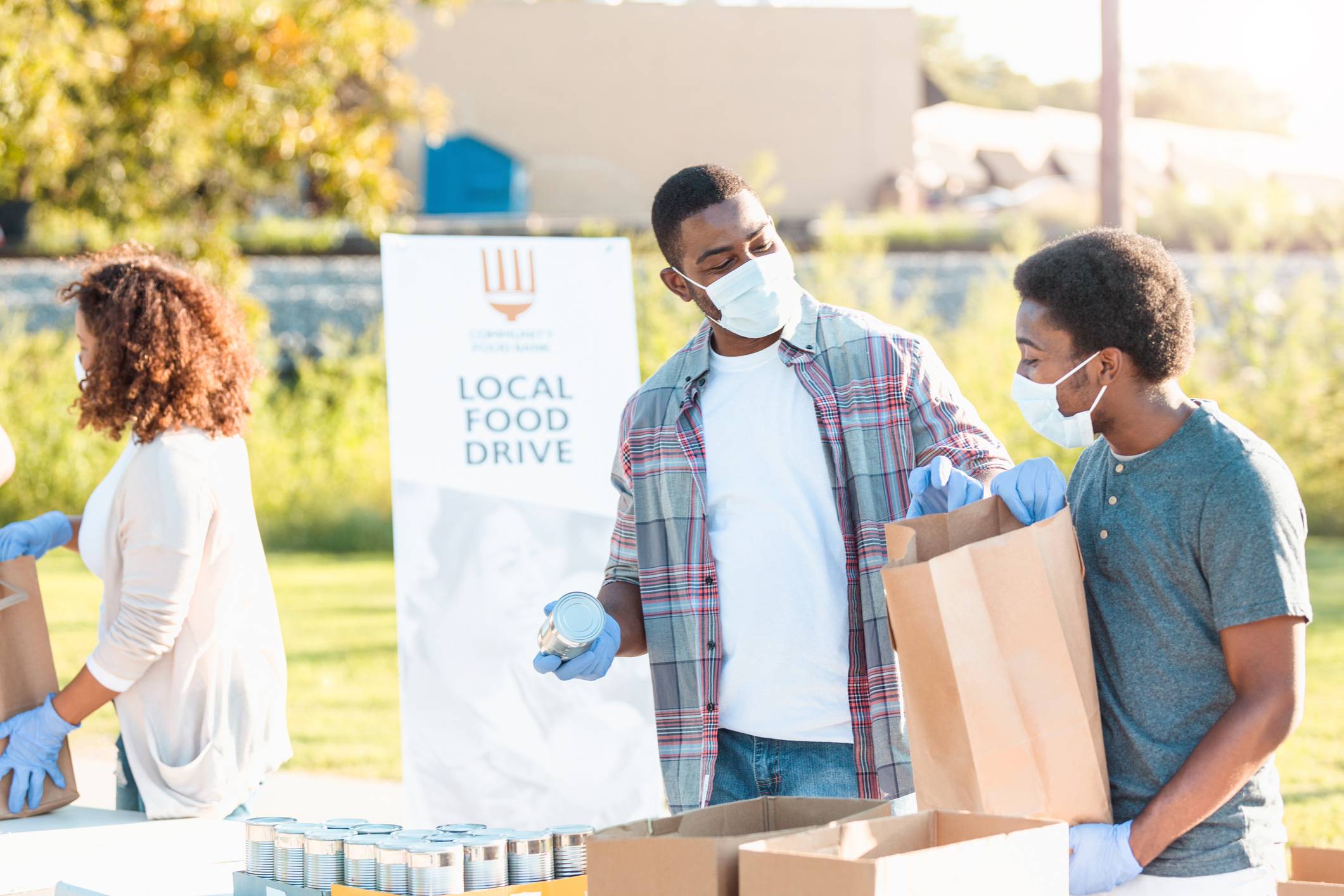 A father and son spend time together sorting food for the community food drive during COVID-19.  They wear protective masks and gloves.