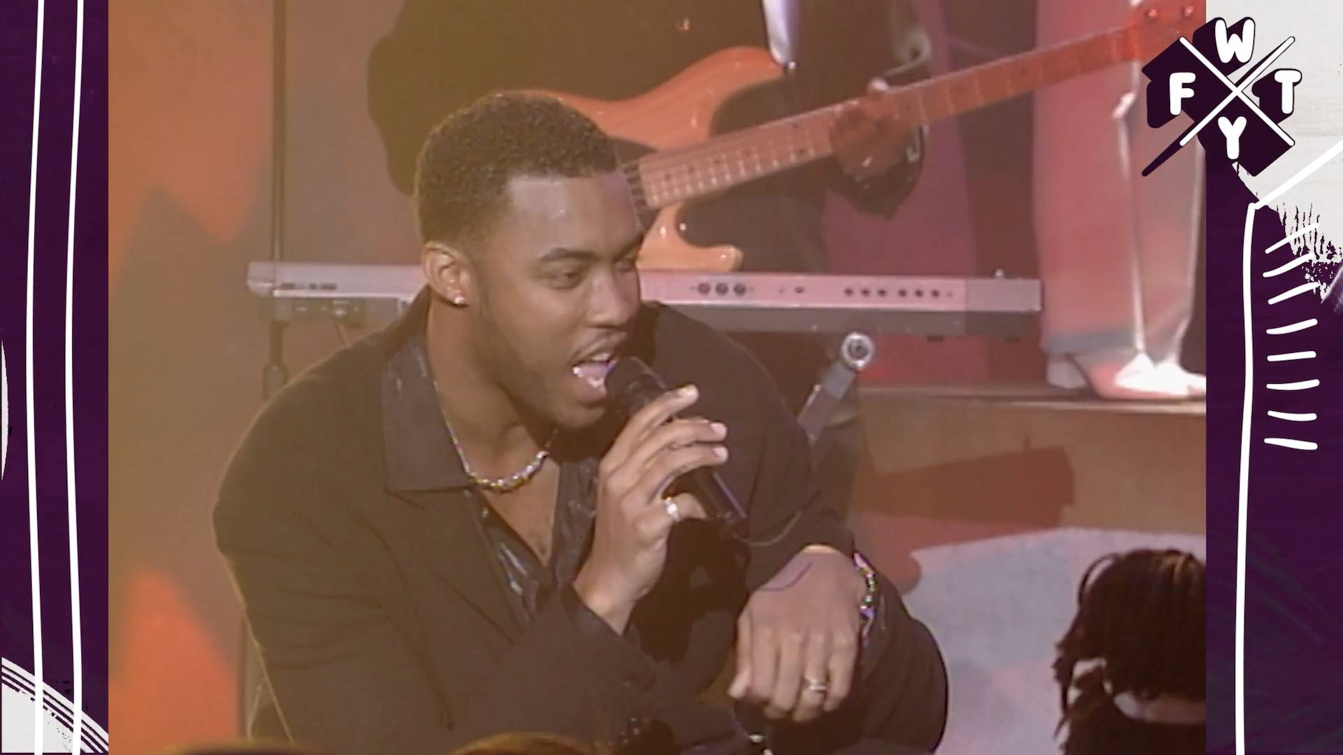 Montell Jordan performing in a black jacket and shirt on stage.
