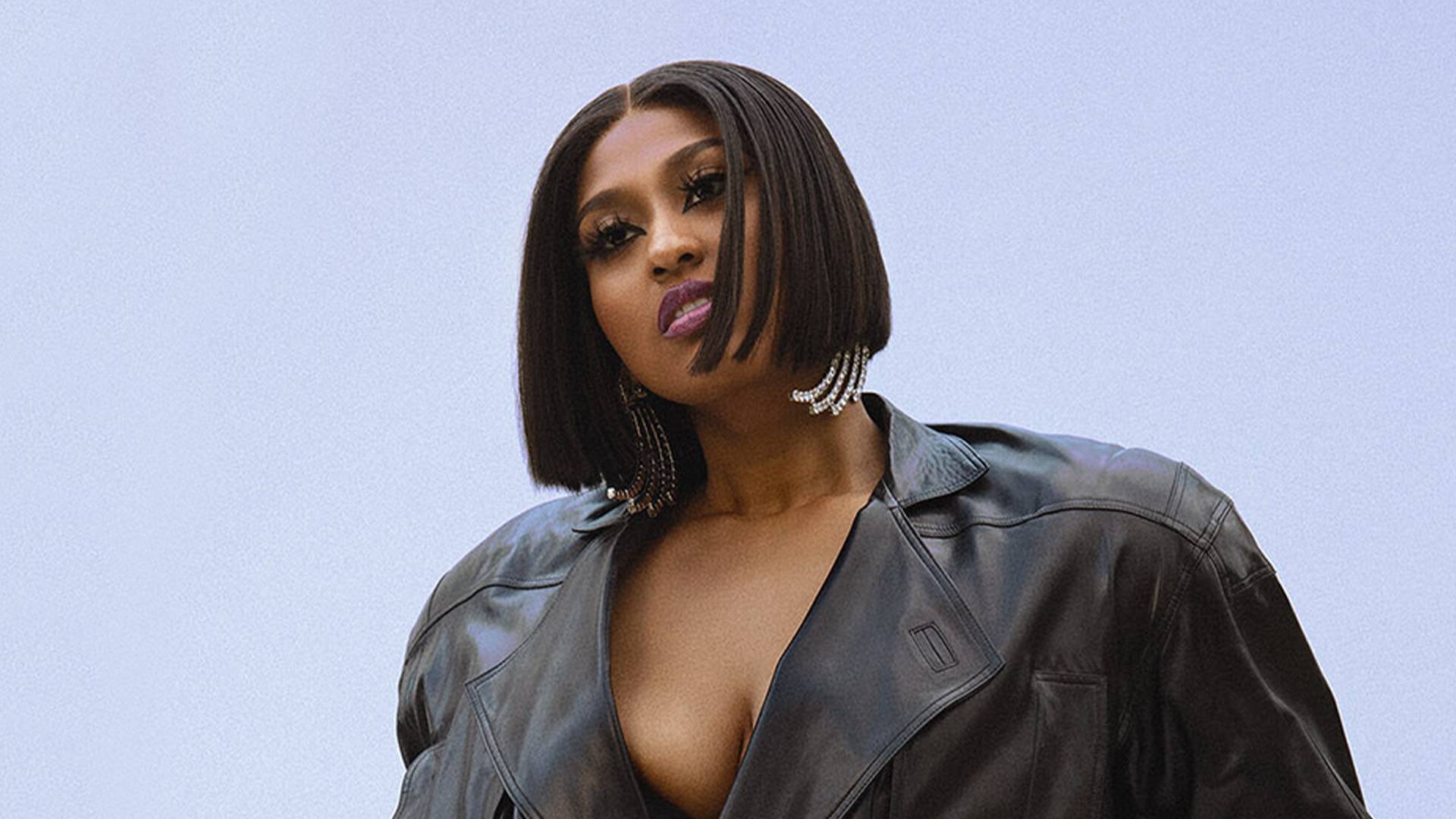 Jazmine Sullivan wearing a black, leather jacket, against a blue background.