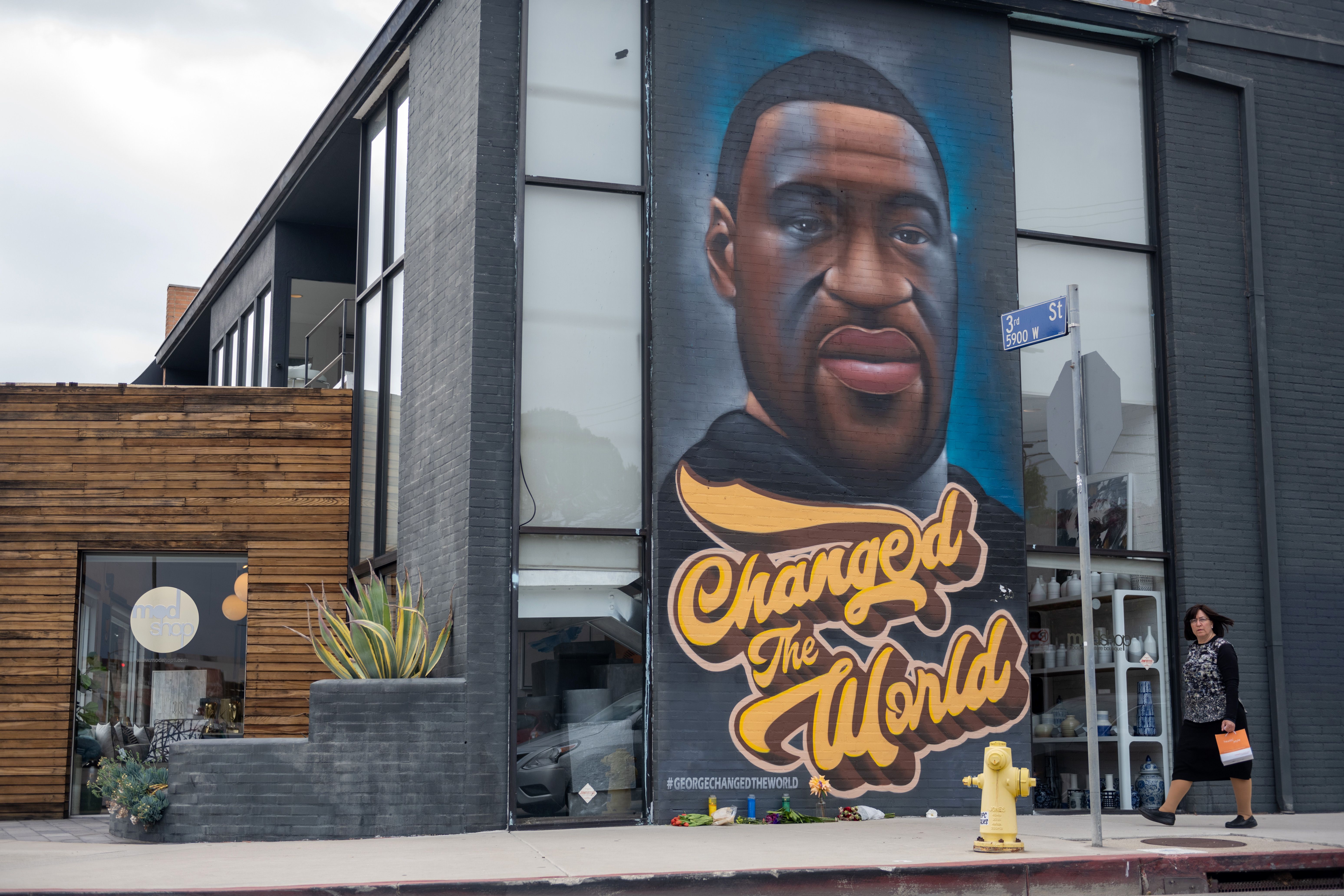 LOS ANGELES, CALIFORNIA - APRIL 21: A woman without a mask walks past a mural of George Floyd that reads, "changed the world" amid the coronavirus pandemic on April 21, 2021 in Los Angeles, California. Los Angeles County moved into Covid-19 orange tier restrictions on April 5 allowing increased capacity at restaurants, movie theaters and museums. (Photo by Alexi Rosenfeld/Getty Images)
