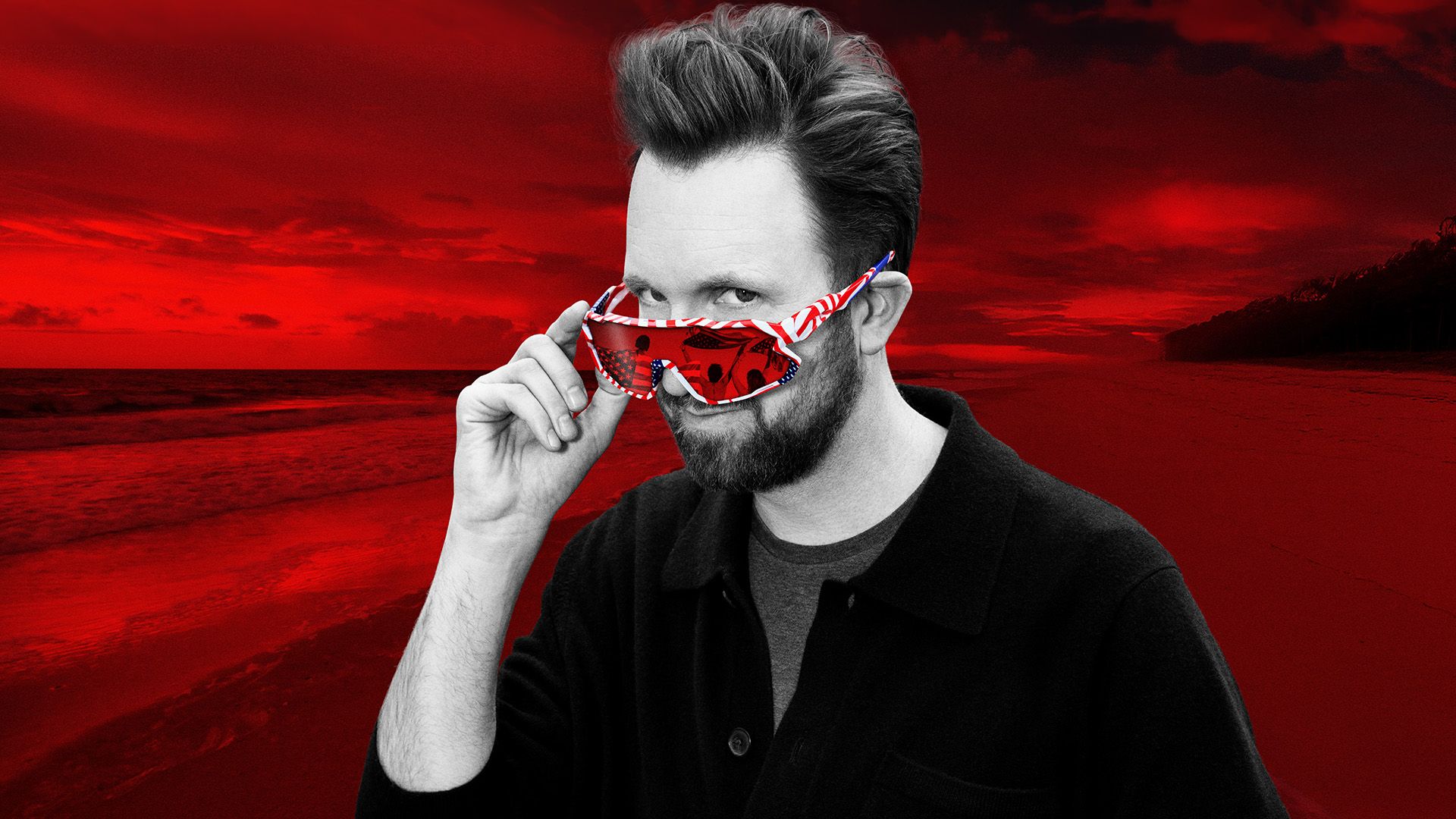 The Daily Show guest host and correspondent Jordan Klepper pictured in black and white over a red-tinted beach background, wearing American-themed single lens sunglasses and peaking over them towards the camera.