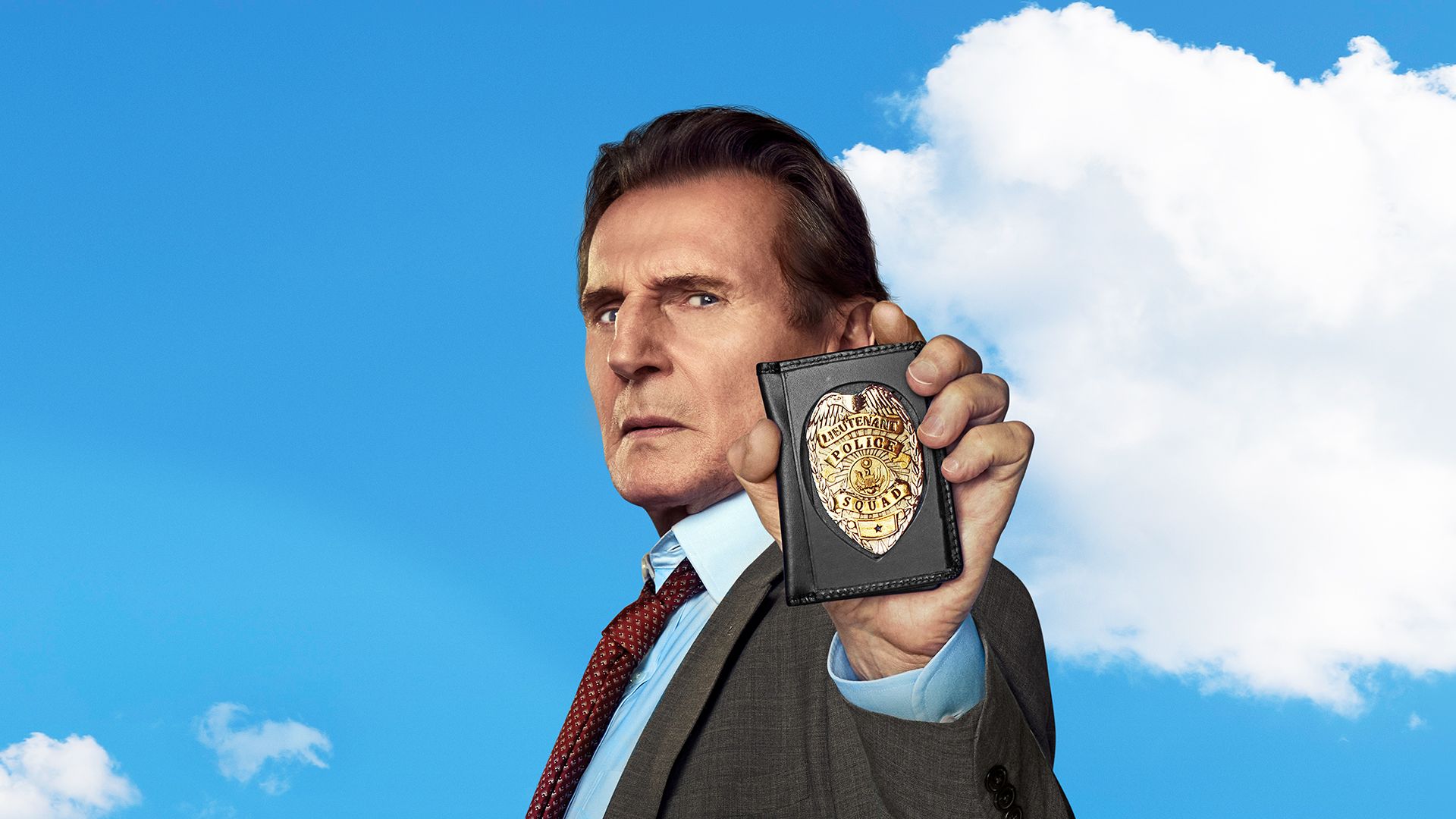 Liam Neeson as Lt. Frank Drebin Jr. in "The Naked Gun" holding his badge up.